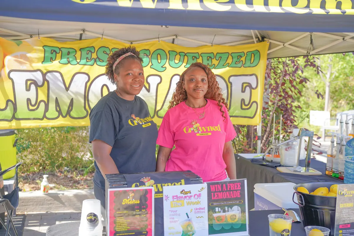 two black women behind a table with product selling lemonade at the farmers' market